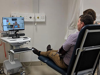 A patient rests on a bed while participating in a telehealth video conference