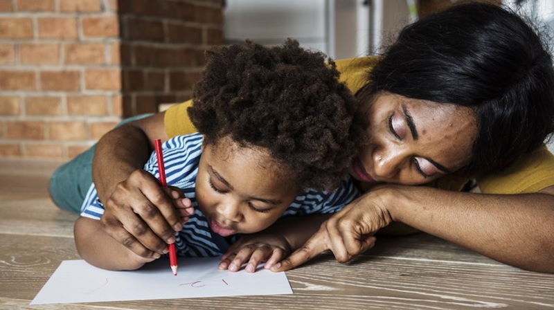 A woman and child practising their writing on a wooden table