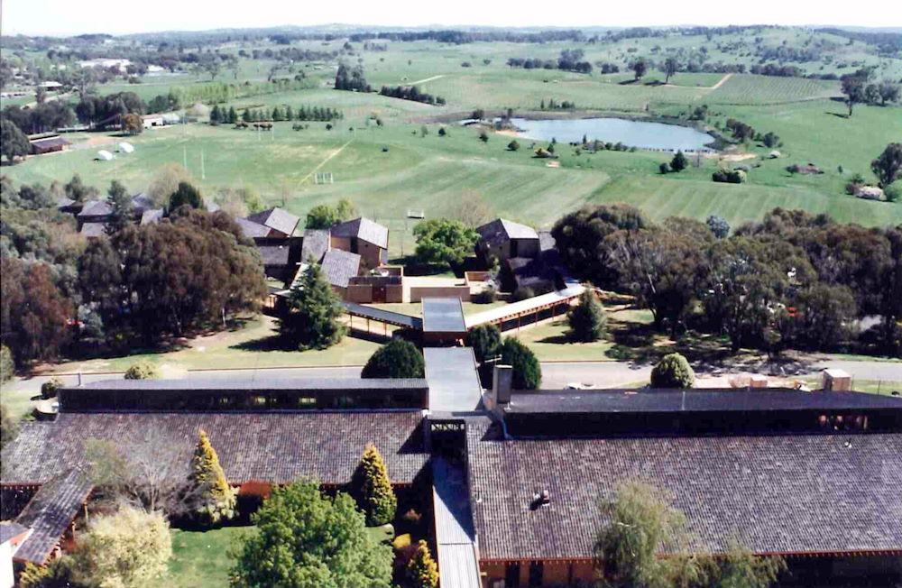 Aerial photo of the campus roofs with fields and a water dam in the background
