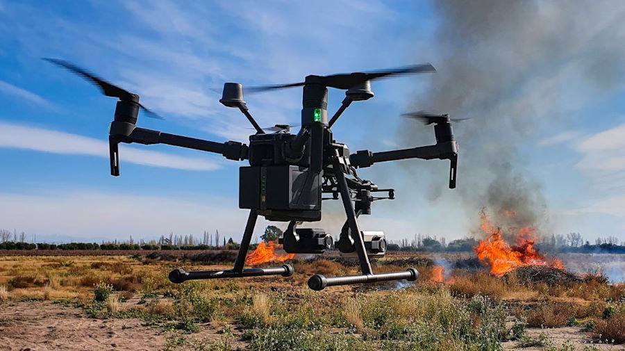 Drone in a field with fire in the distance.