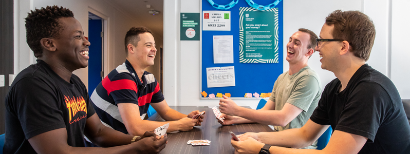 international students in university accommodation sitting together playing cards at a table