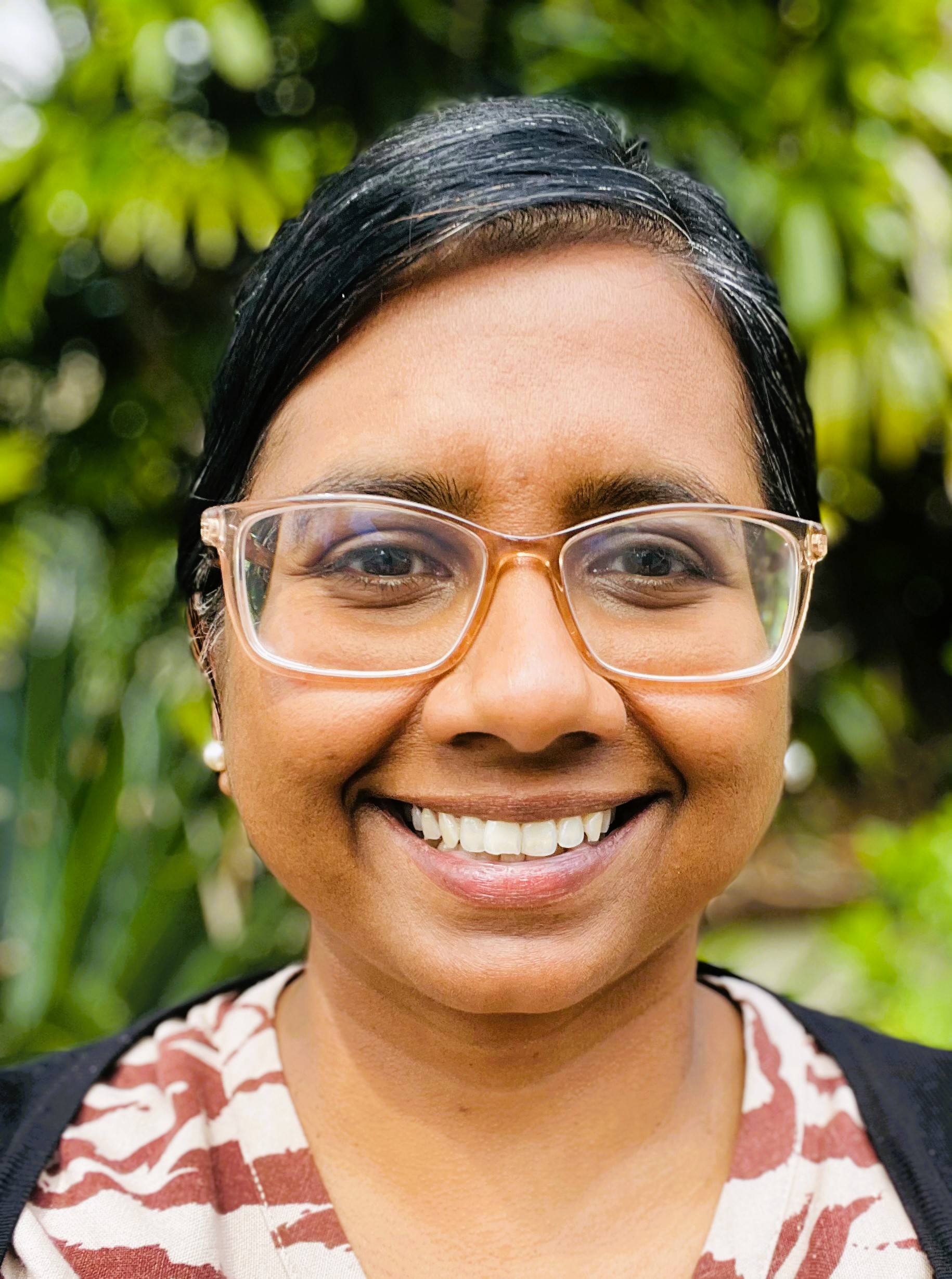 CALD Champion, Koshila Kumar wearing a red and white shirt smiling at the camera. 