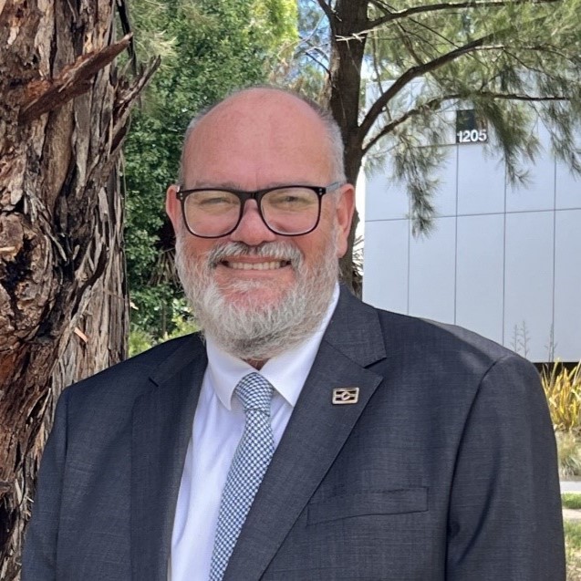 Professor Tony Dreise standing outside wearing a suit and tie smiling. 