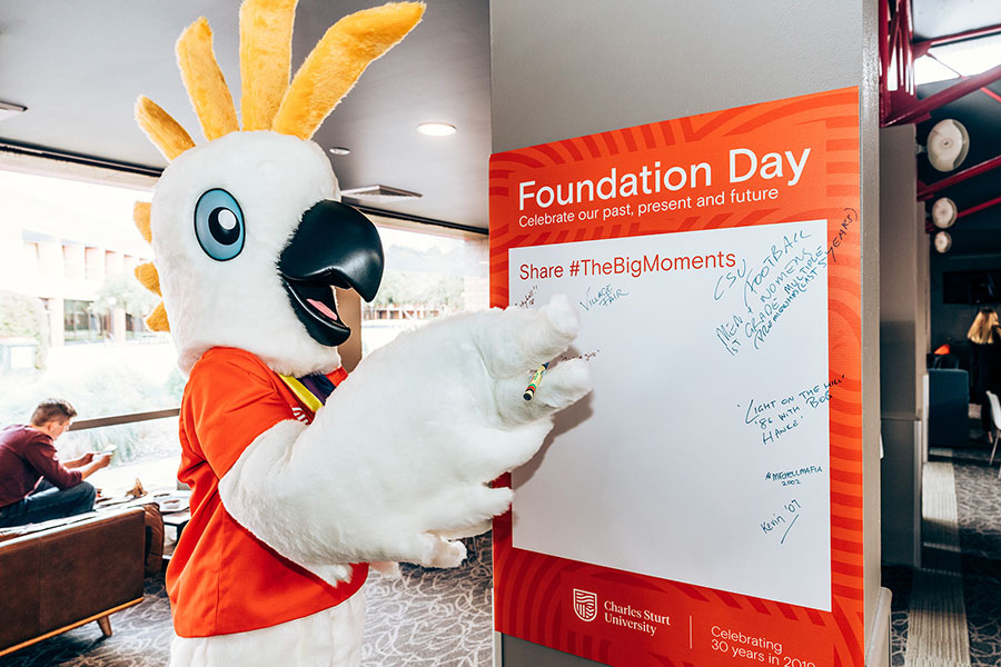 Charlie the mascot writing on a signature board